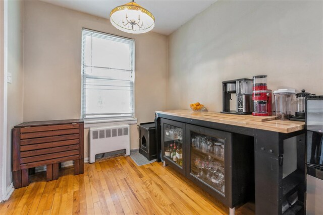 indoor dry bar with radiator heating unit, a chandelier, wood-type flooring, and baseboards
