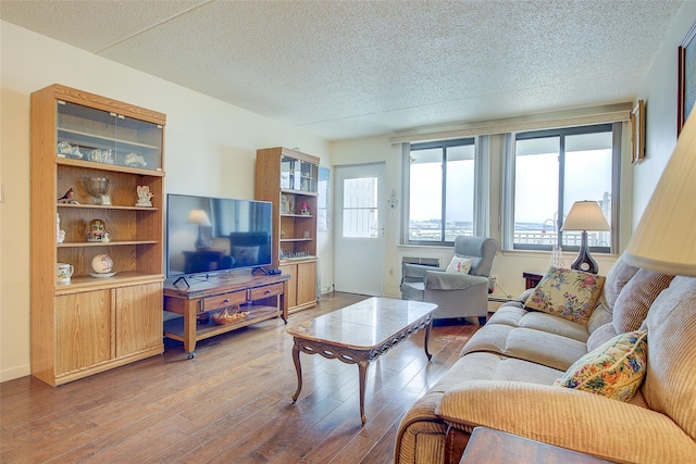 living area featuring healthy amount of natural light, wood finished floors, a textured ceiling, and a baseboard heating unit