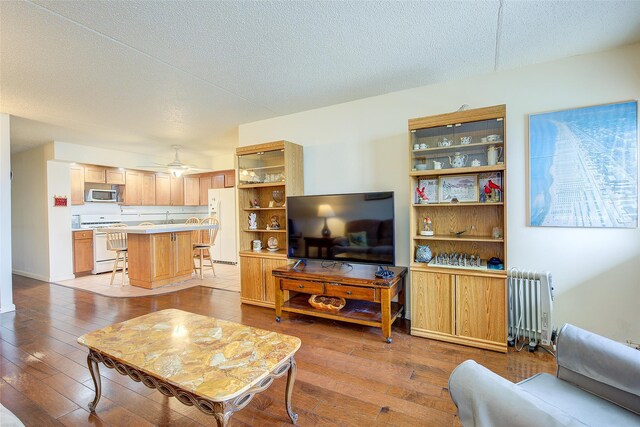 living area featuring radiator, hardwood / wood-style floors, a textured ceiling, and a ceiling fan