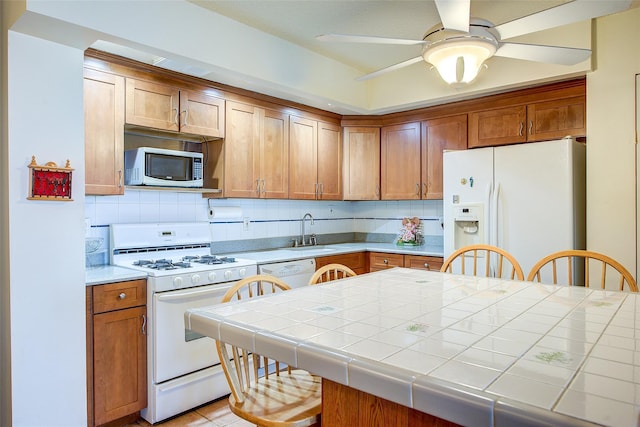 kitchen featuring white appliances, a sink, ceiling fan, backsplash, and tile countertops