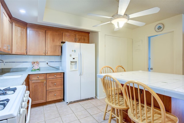 kitchen with white appliances, a sink, brown cabinetry, a ceiling fan, and light tile patterned floors