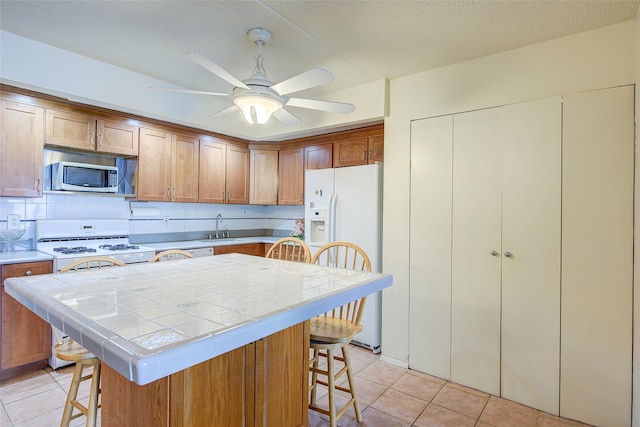 kitchen featuring white appliances, tile counters, a breakfast bar area, a sink, and light tile patterned floors