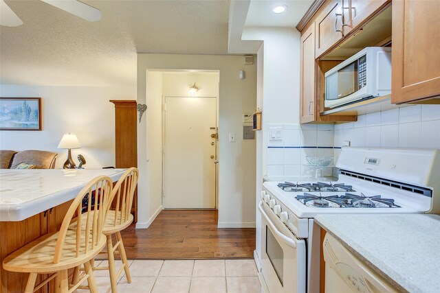 kitchen featuring white appliances, light tile patterned floors, tasteful backsplash, a breakfast bar area, and baseboards
