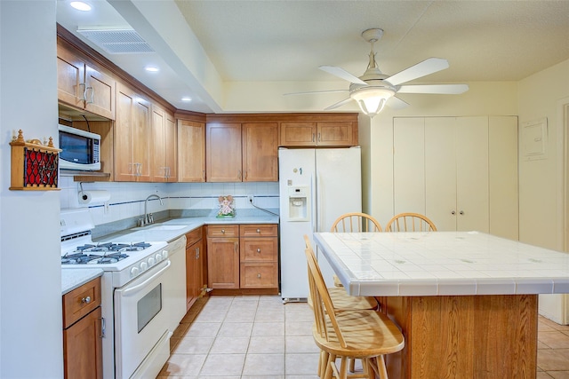kitchen with white appliances, a sink, a kitchen bar, light tile patterned flooring, and ceiling fan