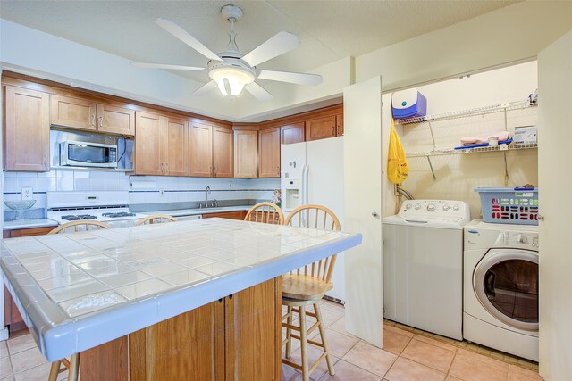 kitchen featuring washing machine and clothes dryer, white appliances, tile countertops, and light tile patterned floors