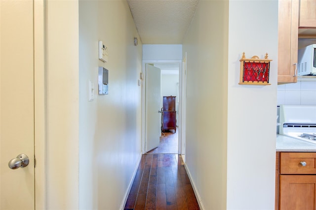 hall featuring baseboards, dark wood-style floors, and a textured ceiling