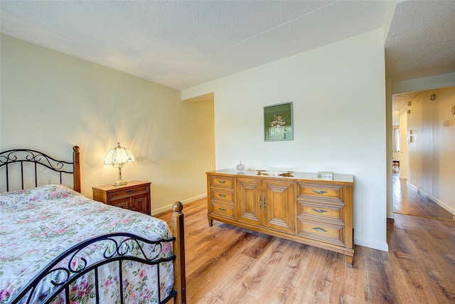 bedroom featuring light wood-type flooring, baseboards, and a textured ceiling