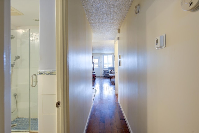 hall with a textured ceiling, dark wood-style flooring, and baseboards