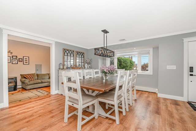 dining room featuring a wood stove, ornamental molding, light wood-type flooring, baseboards, and a chandelier