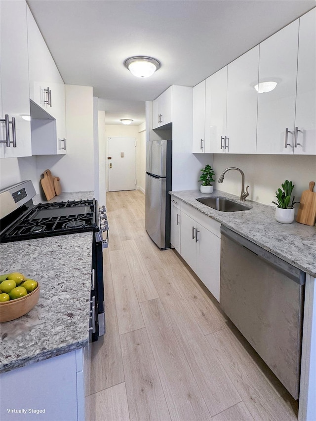 kitchen featuring a sink, appliances with stainless steel finishes, light wood-type flooring, white cabinetry, and light stone counters