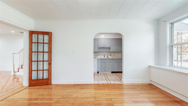 unfurnished dining area with healthy amount of natural light, a sink, light wood-type flooring, and crown molding