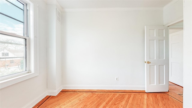empty room with light wood finished floors, ornamental molding, and baseboards