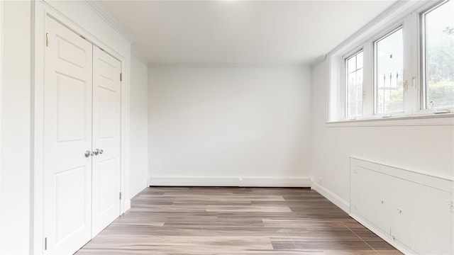 unfurnished bedroom with light wood-style floors, ornamental molding, a baseboard heating unit, a closet, and baseboards