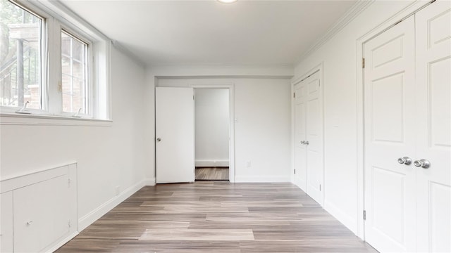 unfurnished bedroom featuring multiple windows, light wood-style floors, a closet, baseboards, and ornamental molding