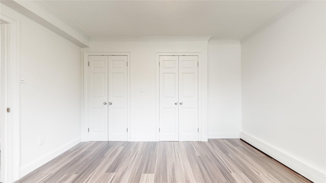 unfurnished bedroom featuring a baseboard radiator, light wood-type flooring, ornamental molding, baseboards, and two closets