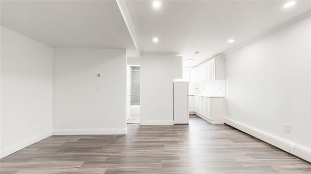 spare room with a baseboard radiator, recessed lighting, light wood finished floors, baseboards, and ornamental molding