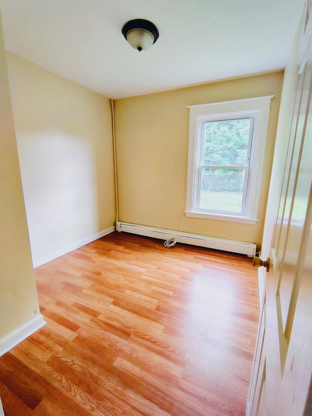 unfurnished room with baseboard heating, light wood-type flooring, and baseboards