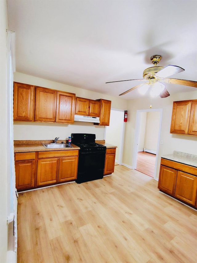 kitchen with black gas range, under cabinet range hood, a sink, brown cabinetry, and light wood-style floors
