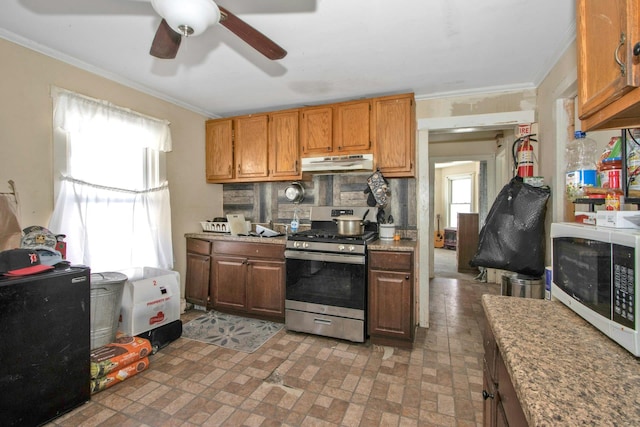 kitchen with stainless steel gas range, white microwave, crown molding, under cabinet range hood, and a ceiling fan
