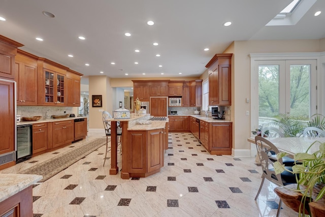 kitchen featuring wine cooler, stainless steel microwave, a kitchen breakfast bar, backsplash, and brown cabinetry