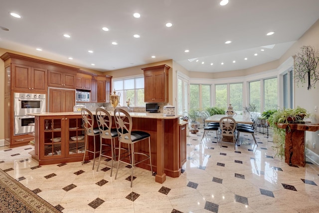 kitchen featuring appliances with stainless steel finishes, recessed lighting, a peninsula, tasteful backsplash, and a kitchen breakfast bar
