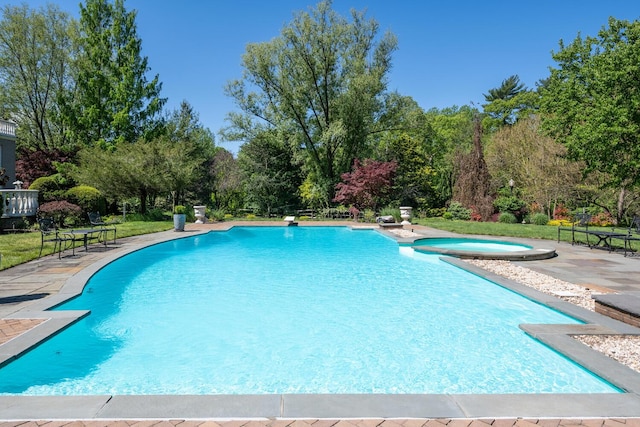 view of swimming pool with a patio, view of wooded area, and a pool with connected hot tub