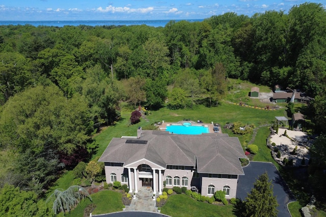 aerial view of property and surrounding area with a heavily wooded area and a nearby body of water