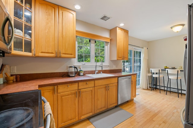 85 Mowbray St, Patchogue, NY 11772 - kitchen with appliances with stainless steel finishes, light wood-style floors, glass insert cabinets, a baseboard heating unit, and recessed lighting