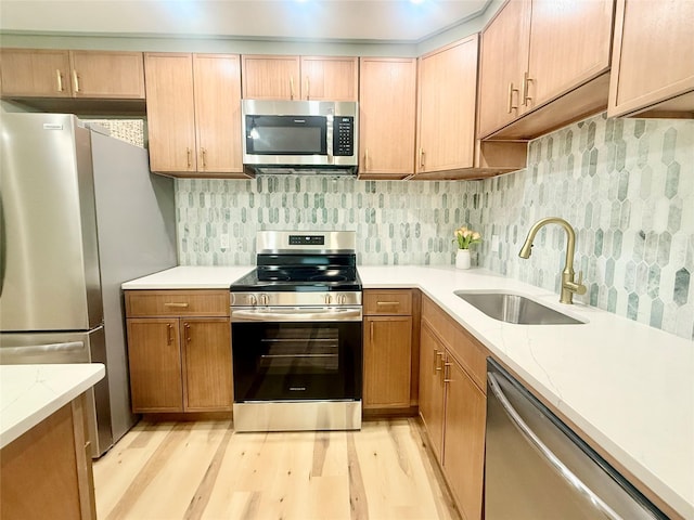 kitchen featuring stainless steel appliances, a sink, light wood-style flooring, and light stone countertops