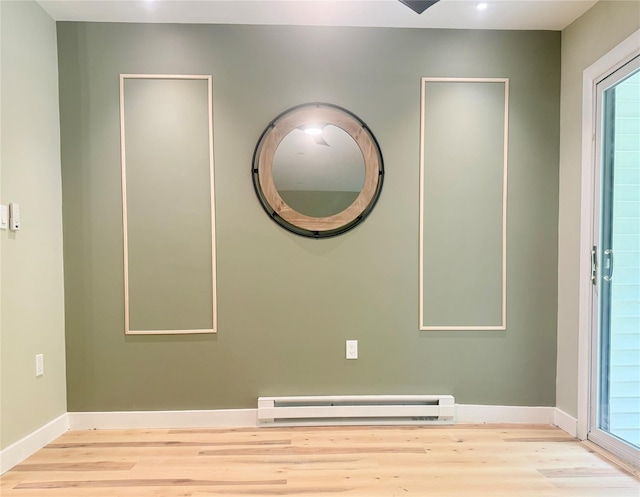 empty room with a baseboard radiator, wood finished floors, baseboards, and healthy amount of natural light