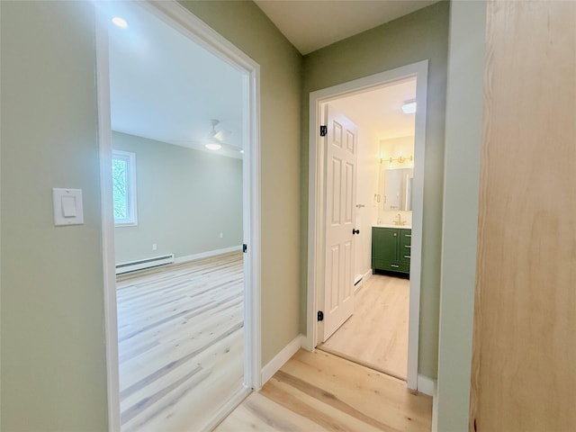 corridor featuring a baseboard heating unit, light wood-type flooring, and baseboards