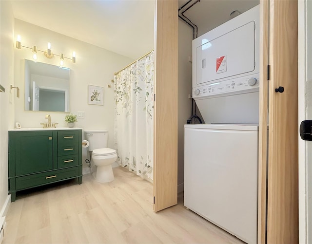 full bath with stacked washing machine and dryer, wood finished floors, toilet, and vanity