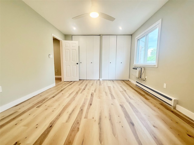 unfurnished bedroom with a baseboard radiator, two closets, a wall mounted air conditioner, light wood-style floors, and baseboards