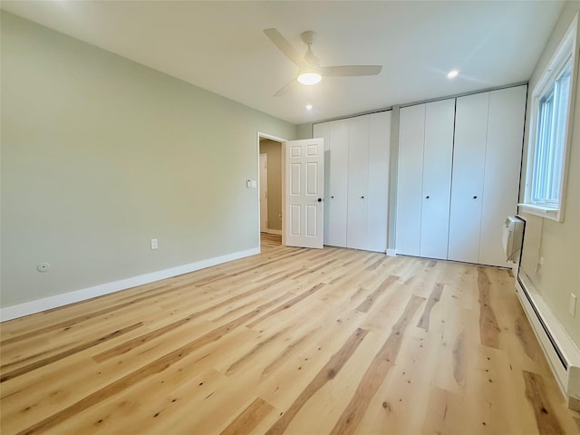unfurnished bedroom featuring multiple closets, baseboard heating, light wood finished floors, a ceiling fan, and an AC wall unit