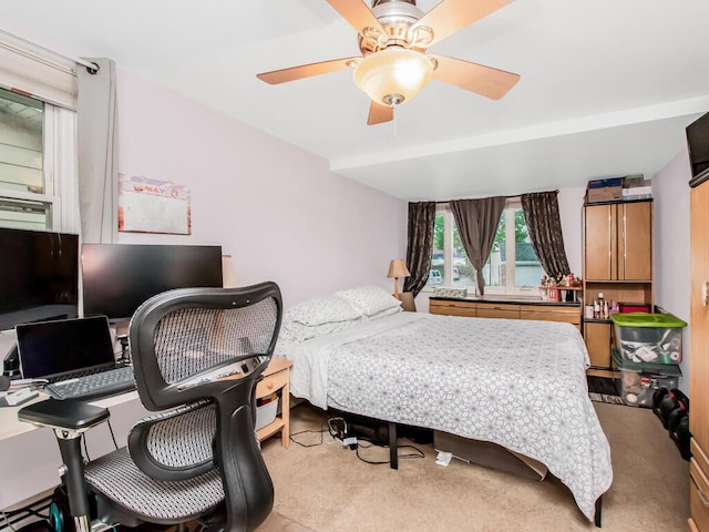 bedroom featuring an office area, light colored carpet, and ceiling fan