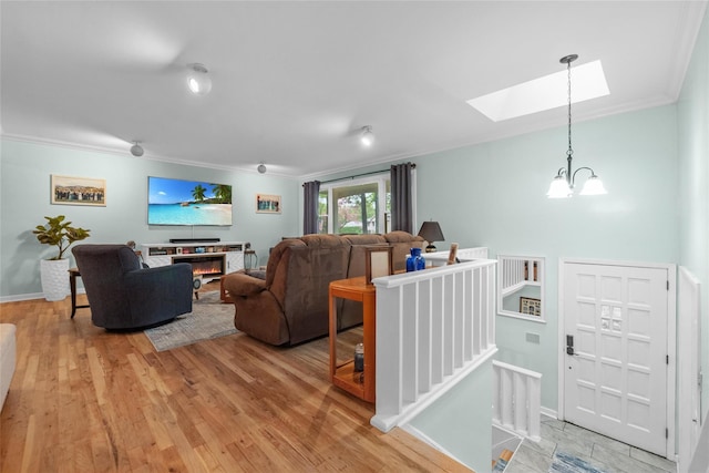 living room featuring a skylight, ornamental molding, light wood-type flooring, baseboards, and a glass covered fireplace