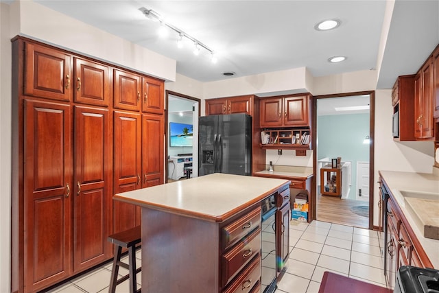 kitchen with black fridge with ice dispenser, light countertops, light tile patterned flooring, a center island, and recessed lighting