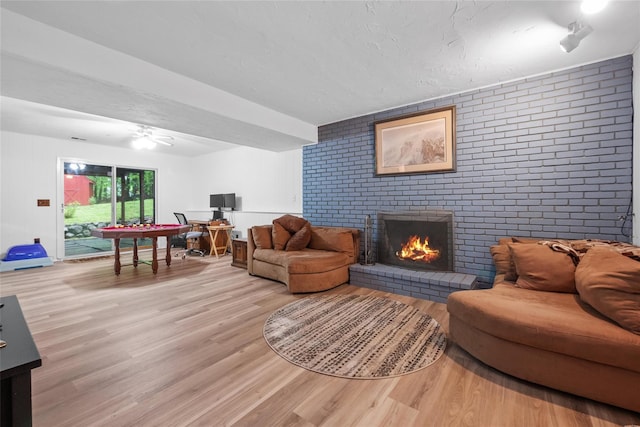 living area featuring light wood-style floors, a fireplace, brick wall, ceiling fan, and a textured ceiling