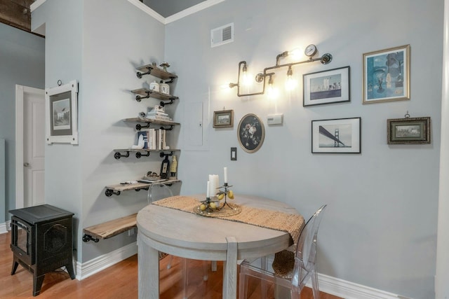 dining room featuring light wood-style flooring, baseboards, a wood stove, and ornamental molding