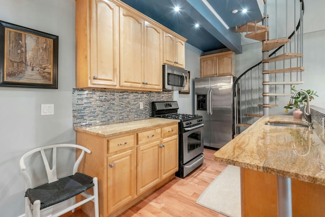 kitchen with appliances with stainless steel finishes, a sink, light brown cabinetry, light wood-type flooring, and decorative backsplash