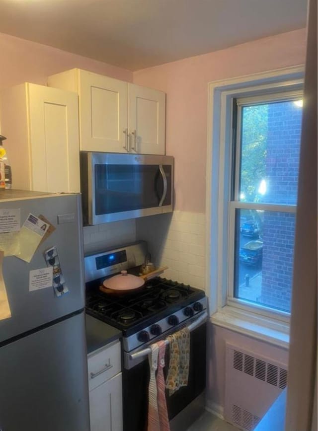 kitchen featuring appliances with stainless steel finishes, radiator, white cabinets, and dark countertops