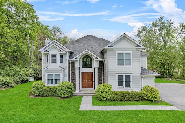 traditional home featuring a front yard, a chimney, roof with shingles, and stone siding