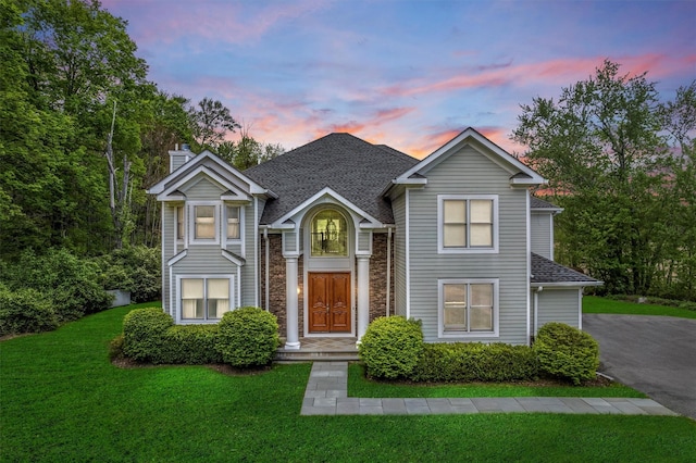 traditional home with a lawn, a chimney, and a shingled roof