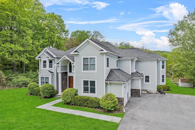 view of front of home with driveway, a shingled roof, a front yard, and stone siding