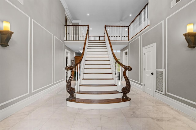 staircase featuring a decorative wall, marble look tiles, a towering ceiling, and recessed lighting