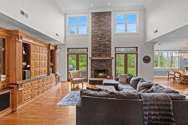 living room featuring crown molding, light wood-type flooring, plenty of natural light, a high ceiling, and a stone fireplace
