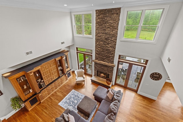 living area featuring a fireplace, wood finished floors, baseboards, ornamental molding, and a towering ceiling