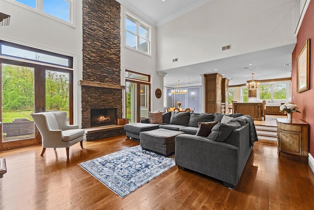 living area with a chandelier, healthy amount of natural light, wood finished floors, a towering ceiling, and crown molding