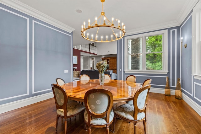 dining room with wood finished floors, a chandelier, crown molding, baseboards, and a decorative wall