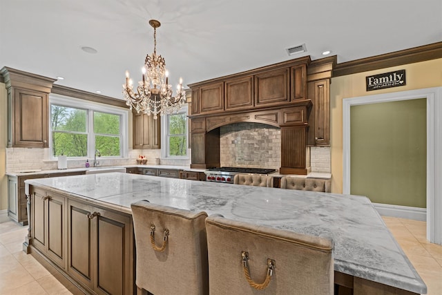 kitchen with a chandelier, a sink, light tile patterned floors, light stone counters, and decorative backsplash
